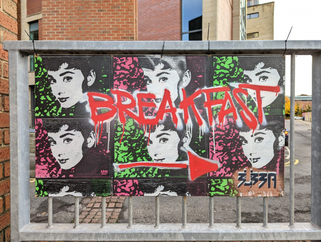 Artwork attached to railings with images of Audrey Hepburn and the word 'Breakfast' sprayed across it with an arrow pointing right