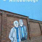 Mural of two faceless elderly Sheffield Wednesday fans photographed from a distance with the stands in the background